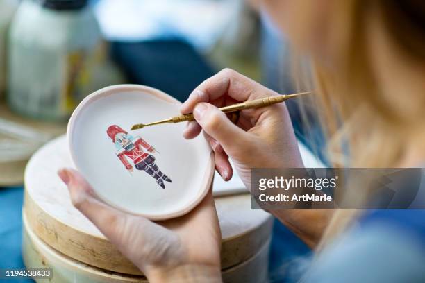 junge frau malerei nussknacker auf weihnachten keramik in ihrer töpferwerkstatt, kleines business-konzept - keramiker stock-fotos und bilder