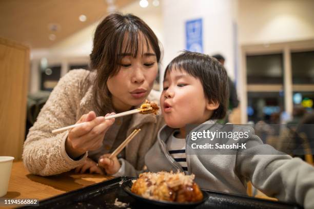 la giovane madre e il suo figlio piccolo che soffiano a takoyaki prima di mangiare, - japanese restaurant foto e immagini stock