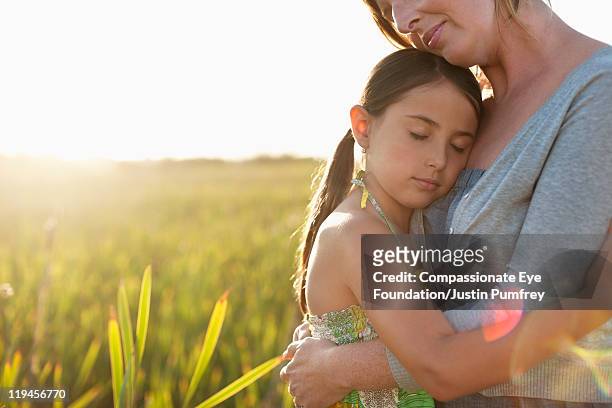 mother and daughter embracing in a field - compassionate eye foundation stock-fotos und bilder