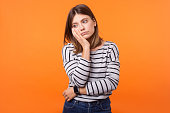 Portrait of bored young woman with brown hair in long sleeve striped shirt. indoor studio shot isolated on orange background