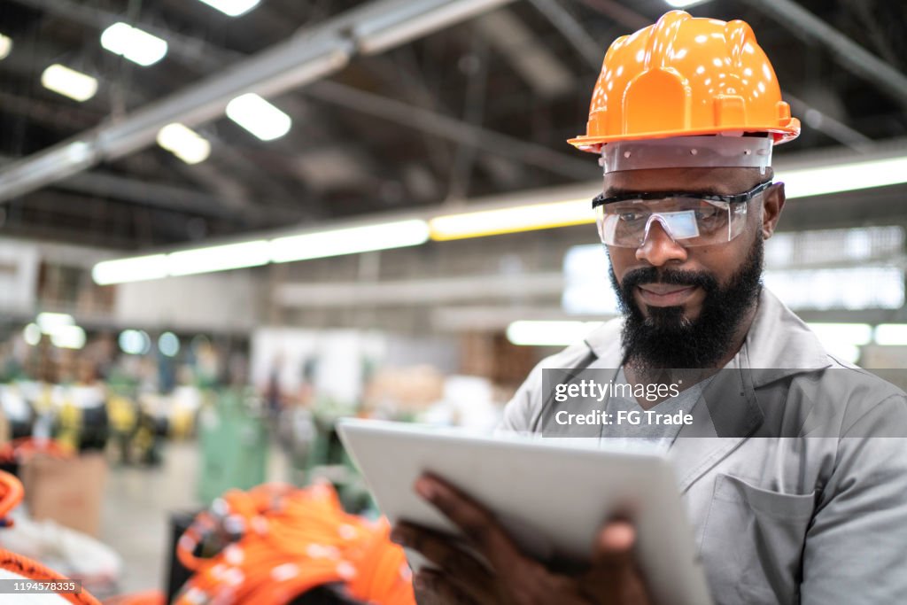 Homem que trabalha com sua tabuleta digital na fábrica