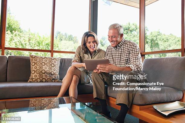 mature couple sitting on sofa using digital tablet - compassionate eye foundation stock-fotos und bilder