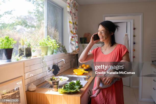 one woman on the phone with a young baby making a salad in the kitchen - showus family stock pictures, royalty-free photos & images