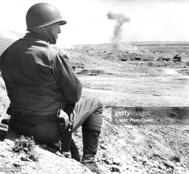 American military commander Lieutenant General George S. Patton sits on the sand and watches a tank battle in Tunisia, 1943.