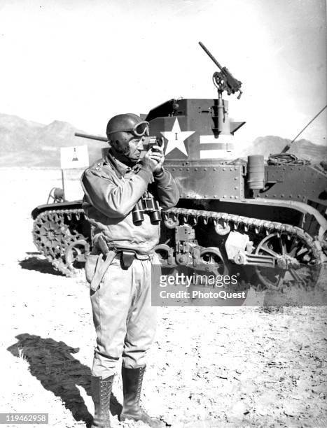 American military commander General George S. Patton checks range as he stands next to a tank during training maneuvers, 1942.