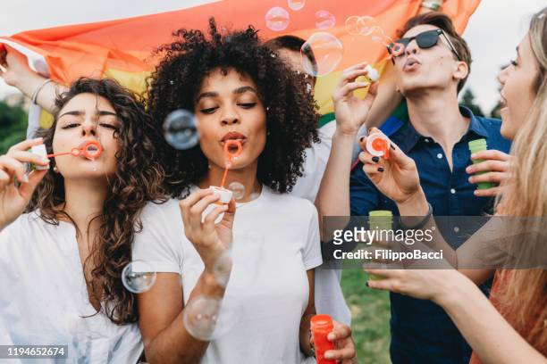 vrienden die plezier hebben met zeepbellen samen in het park - party flags stockfoto's en -beelden
