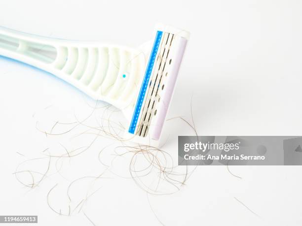 close up of disposable blue razor with hairs between the blades on a white background - pubic hair stock pictures, royalty-free photos & images