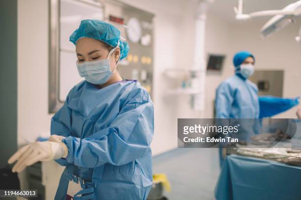 eine asiatische chinesische chirurgin arzt trägt chirurgische handschuhe vor der operation im operationssaal - operationskittel stock-fotos und bilder
