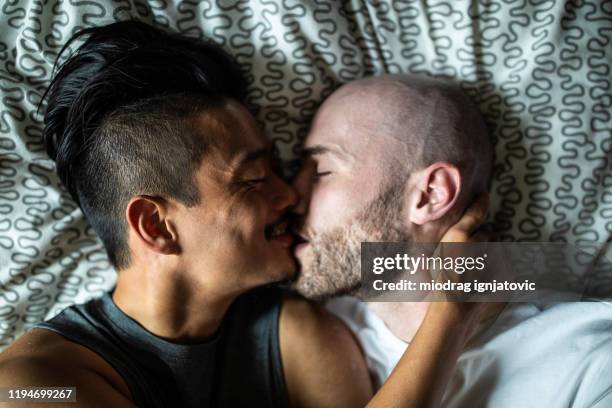 encantadora pareja gay besándose en la cama - beso en la boca fotografías e imágenes de stock