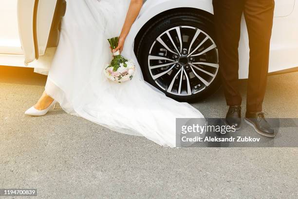 stylish and fashionable newlyweds stand near an expensive white car in the summer. in the hands of the bride wedding bouquet. - car appearance stock pictures, royalty-free photos & images