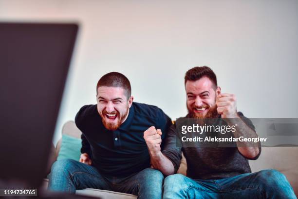 twee mannelijke sport fans genieten van gespannen voetbalwedstrijd - man watching tv on couch stockfoto's en -beelden