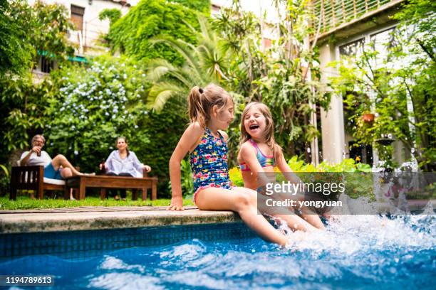 zwei kleine mädchen sitzen am pool und spritzen wasser mit beinen - kinder schwimmbad stock-fotos und bilder