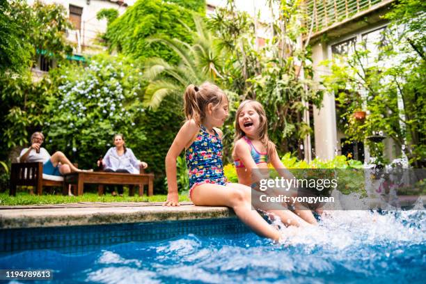 dos niñas sentadas junto a la piscina y salpicando agua con piernas - water garden fotografías e imágenes de stock