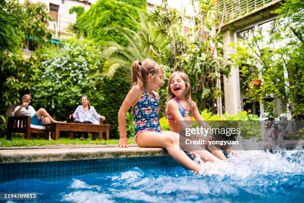 deux petites filles s'asseyant au bord de la piscine et éclaboussant l'eau avec des jambes - piscine photos et images de collection