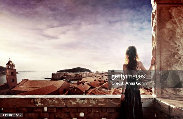 rear view of redhead in strapless dress leaning against castle wall, composited with background of battlements of dubrovnik old town, croatia - princess castle stock pictures, royalty-free photos & images