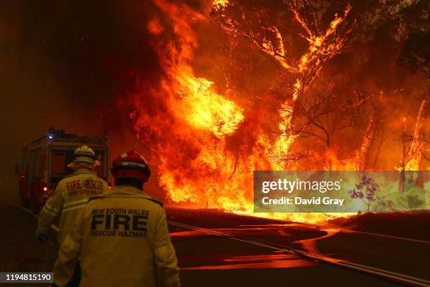 Fire and Rescue personnel run to move their truck as a bushfire burns next to a major road and homes on the outskirts of the town of Bilpin on...
