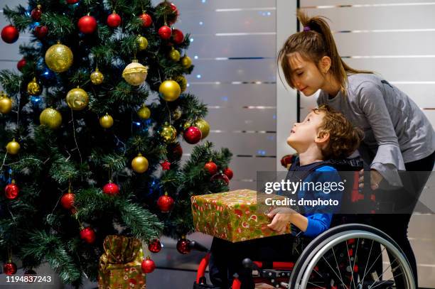 little boy in wheelchair and his sister opening christmas gifts - sibling hospital stock pictures, royalty-free photos & images