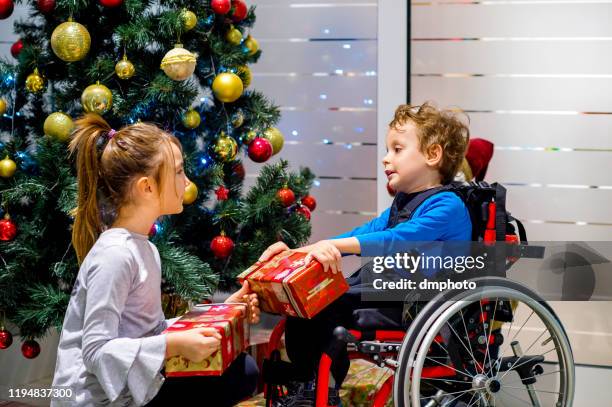 little boy in wheelchair and his sister opening christmas gifts - kids hospital christmas stock pictures, royalty-free photos & images