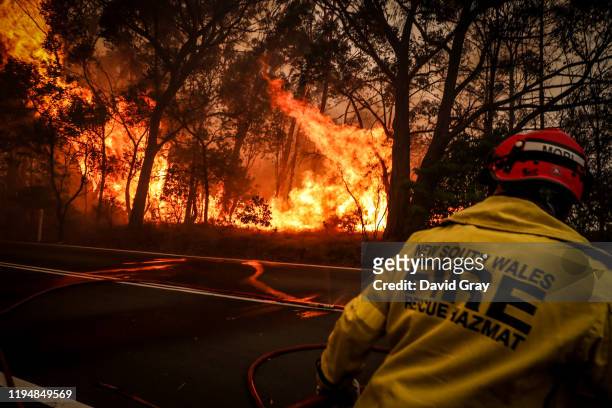 Fire and Rescue personnel run from flames as a bushfire burns trees along a road near homes on the outskirts of the town of Bilpin on December 19,...