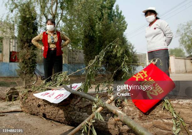 Two peasant women, wearing masks, man a barricade with a sawn-off tree blocking the road into their village that located near the hospital erected...