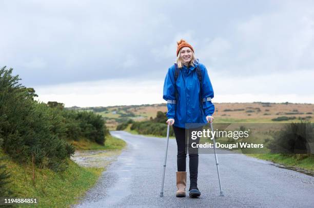 positive female hiker with crutches on a rural country lane. - krücke stock-fotos und bilder