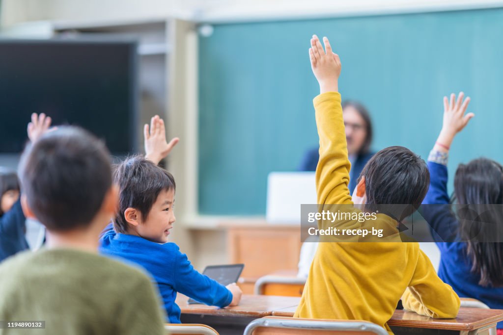 Rear view of group of school children while raising their hands