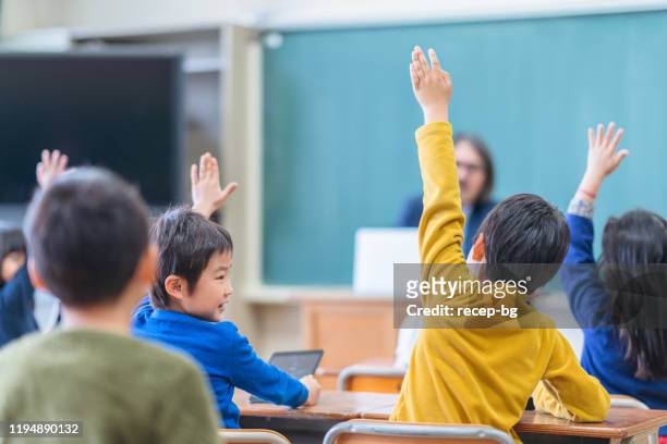 rear view of group of school children while raising their hands - elementary school building stock pictures, royalty-free photos & images