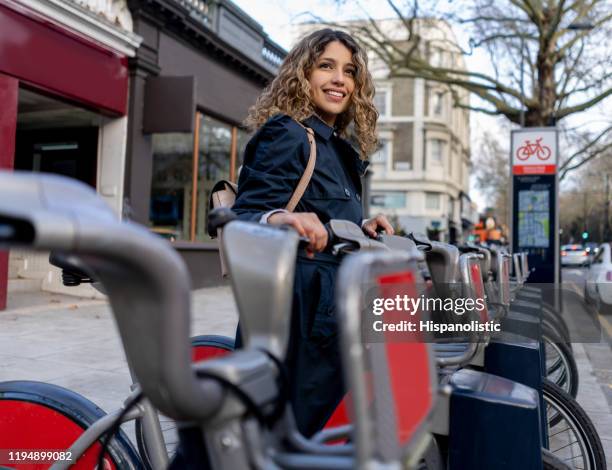 mooie jonge vrouw het huren van een stadsfiets glimlachend - bicycle rental stockfoto's en -beelden