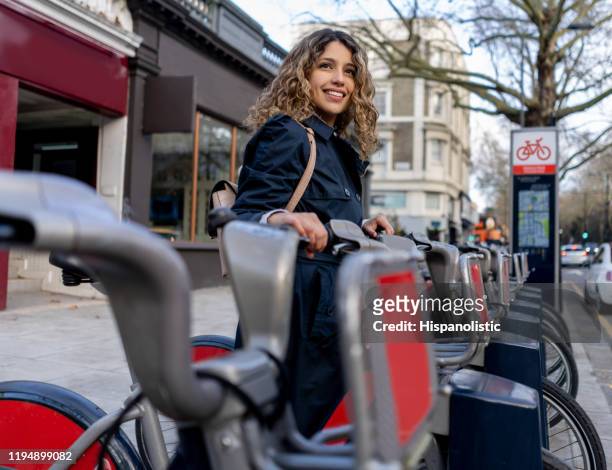beautiful young woman renting a city bicycle smiling - bike sharing stock pictures, royalty-free photos & images