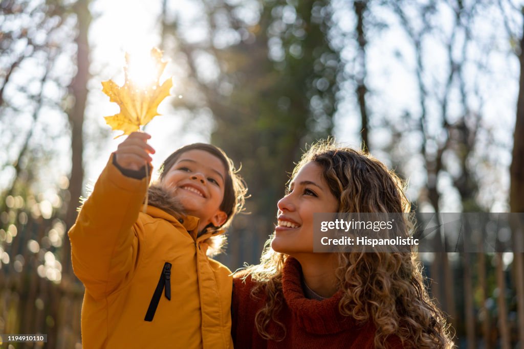 美麗的母親看著一片葉子，她的兒子在公園裡一個陽光明媚的秋天舉行