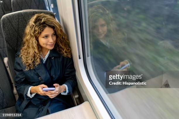 beautiful woman traveling by train looking at the view while texting on smartphone - rail transportation stock pictures, royalty-free photos & images