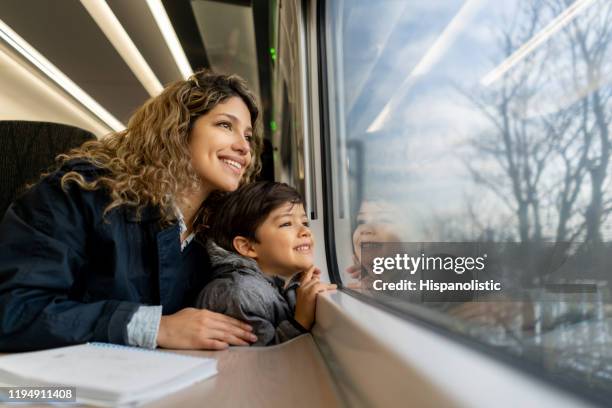 gelukkige alleenstaande moeder en zoon kijken naar het raam uitzicht beide glimlachen tijdens het reizen met de trein - family travel stockfoto's en -beelden