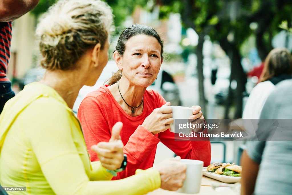Smiling mature female friends enjoying breakfast at outdoor cafe after morning run