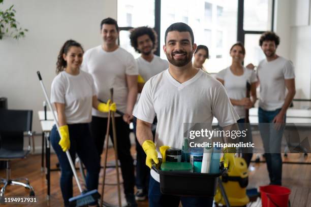 joven alegre parte de un equipo de limpieza sosteniendo una bandeja con productos de limpieza todos sonriendo a la cámara - limpieza profesional fotografías e imágenes de stock