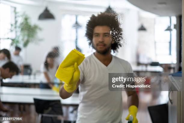 young man part of a cleaning team service at an office cleaning a glass window - cleaning crew stock pictures, royalty-free photos & images