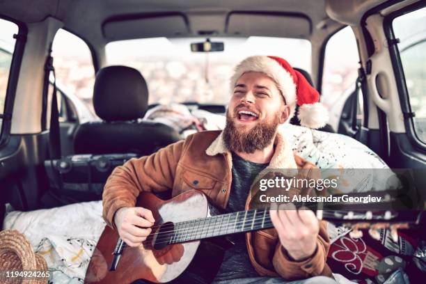 glückliches männchen mit weihnachtsmütze in der rücken von minivan spielen gitarre und singen - auto singen stock-fotos und bilder