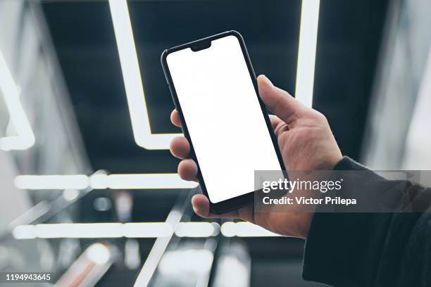 mock up of a smartphone in hand, on the background of an escalator in a shopping center and luminous lamps. - man holding his hand out stockfoto's en -beelden