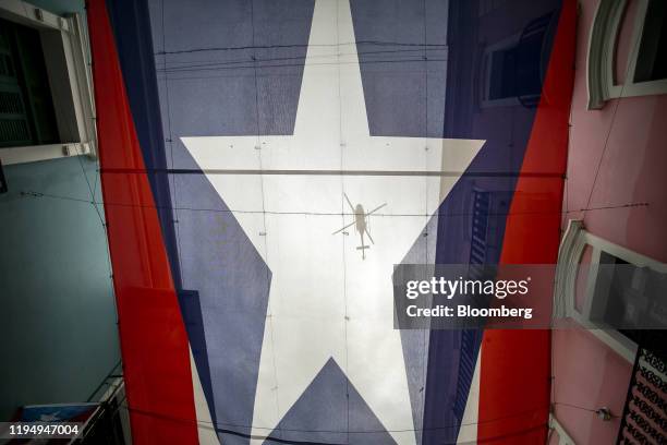 Police helicopter is seen through a Puerto Rican flag as it flies above a protest against the government in San Juan, Puerto Rico, on Monday, Jan....