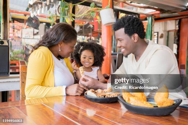 the afro family begins to eat the empanadas and the pork rinds they bring to the restaurant table - cali colombia stock pictures, royalty-free photos & images