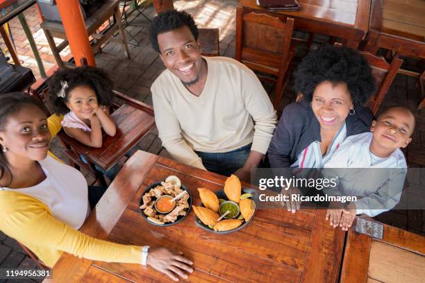 la familia afro comienza a comer las empanadas y las cortezas de cerdo que traen a la mesa del restaurante - cali colombia fotografías e imágenes de stock