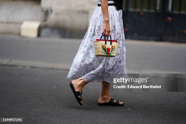 Guest wears a white open-work "broderie anglaise" pleated dress, a small woven straw basket with colorful floral embroideries, black flat sandals,...
