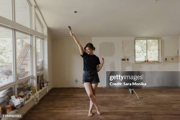 woman holding paintbrush and dancing in new home - happy moment woman stock-fotos und bilder