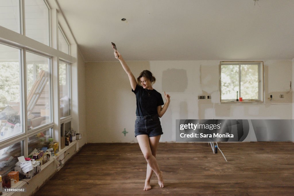 Woman holding paintbrush and dancing in new home