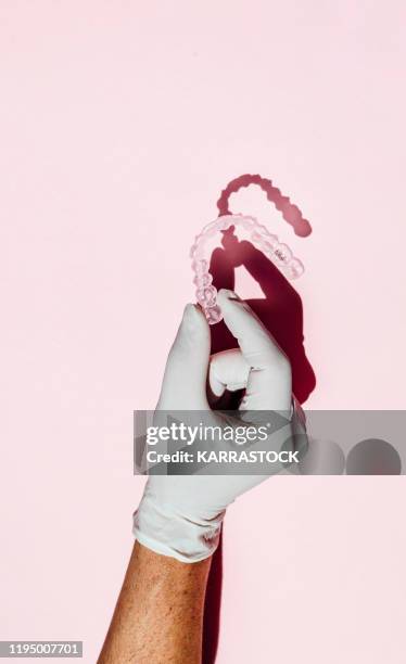 doctor hand holding a clear dental aligner with the pink background - invisible braces stock pictures, royalty-free photos & images