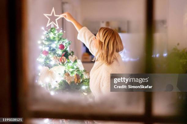 ms woman decorating the christmas tree on idyllic winter day at home, view through frosted window - christmas window stock pictures, royalty-free photos & images