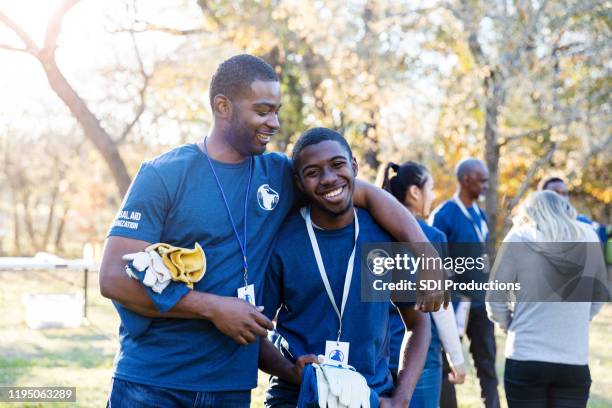 older brother smiles at and puts arm around younger brother - fraternity brother stock pictures, royalty-free photos & images