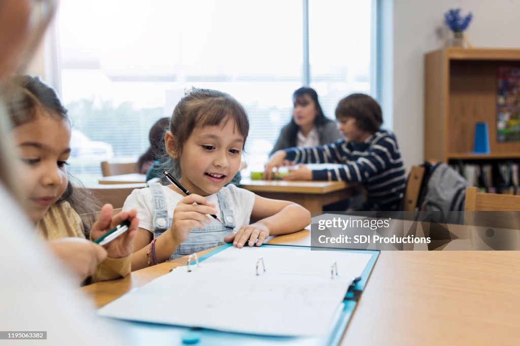 Girl Writing Assignment Elementary Age Girls Work On Writing Assignment As Teacher Watches High ...