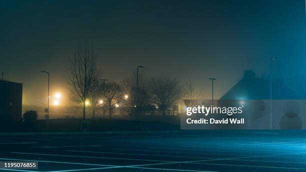 an empty car park with street lights glowing in the distance on a mysterious moody,  foggy atmospheric winters night - david noone stock pictures, royalty-free photos & images