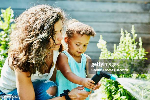 female toddler helping mother water plants in backyard garden on summer morning - hose pipe stock pictures, royalty-free photos & images