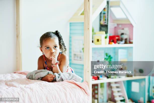 portrait of young girl holding blanket and leaning against bed in bedroom - thumb sucking stock pictures, royalty-free photos & images